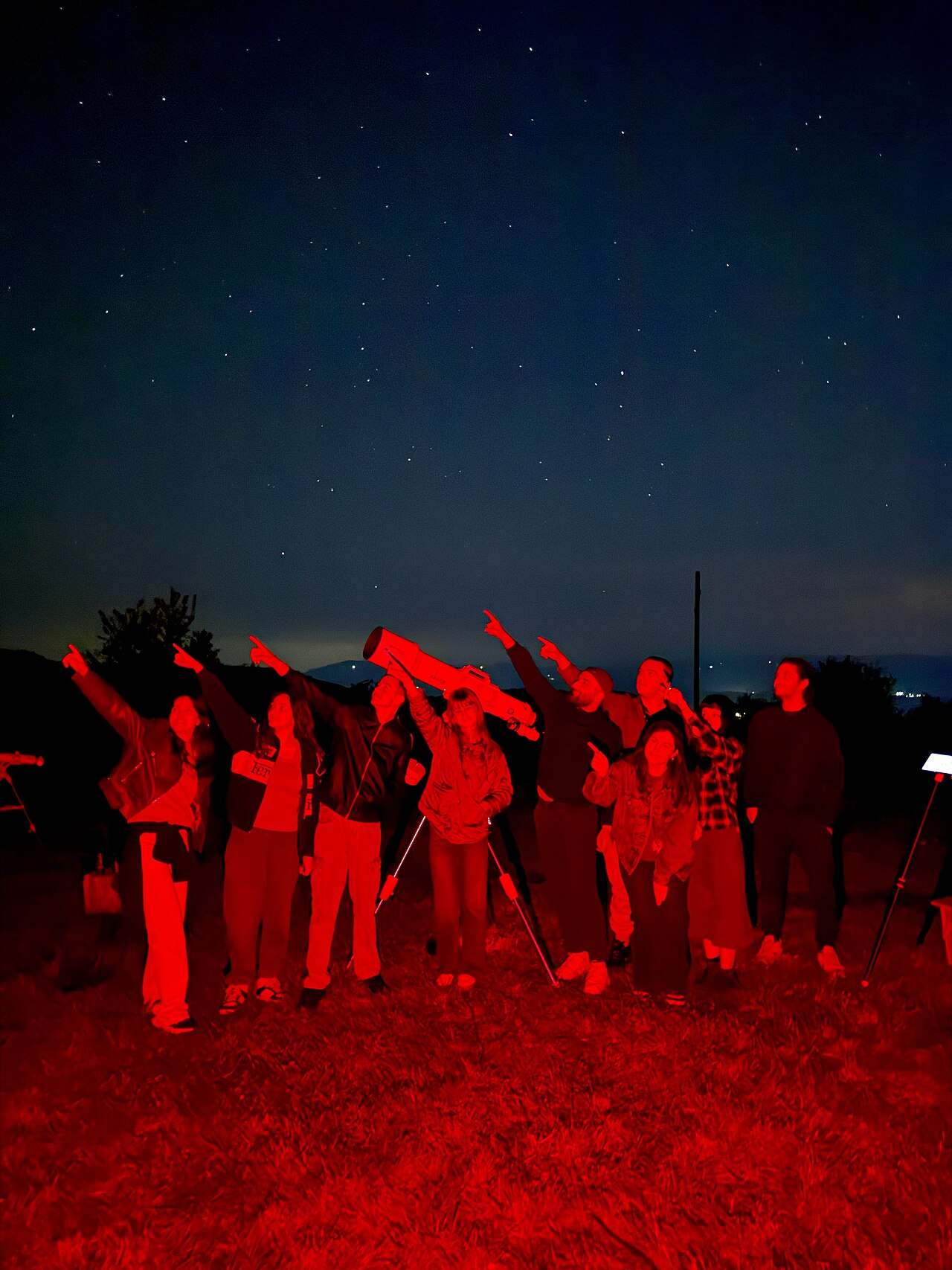 Grupo de personas observando el cielo junto a un telescopio bajo iluminación roja